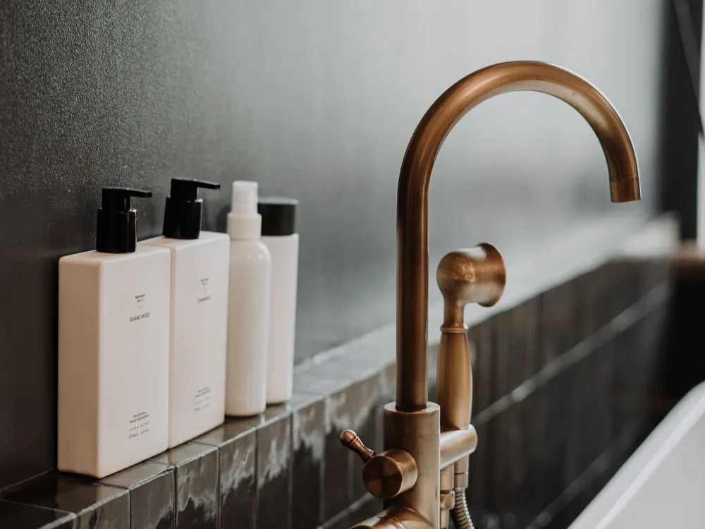 Brushed brass bath tap beside a white bathtub