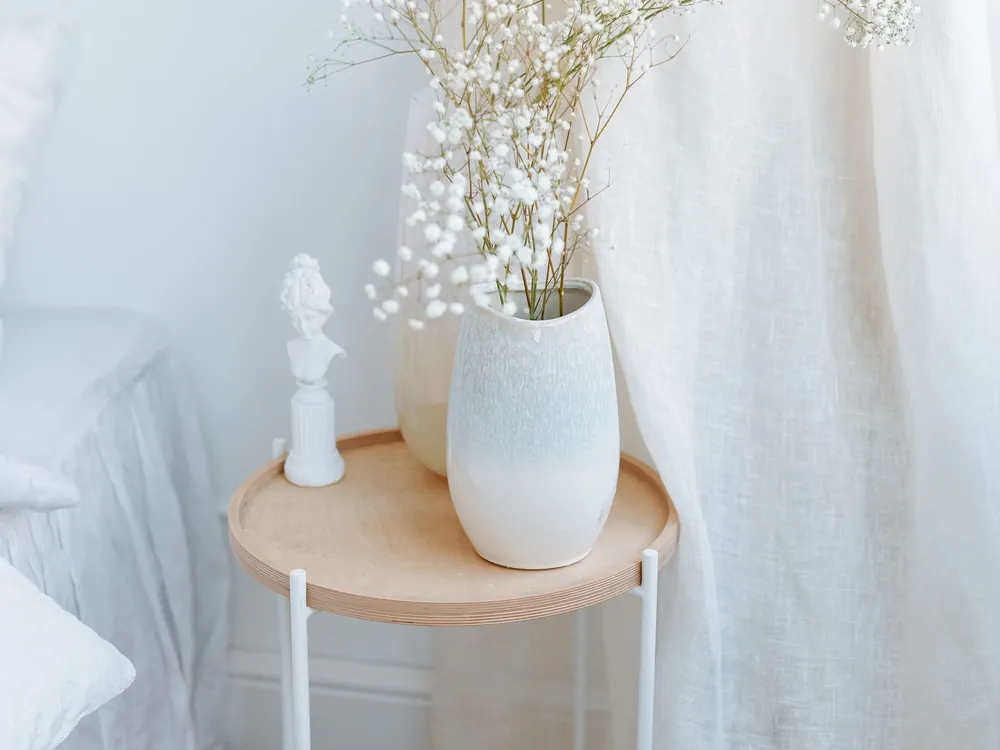 White ceramic vase with baby's breath on a light timber side table
